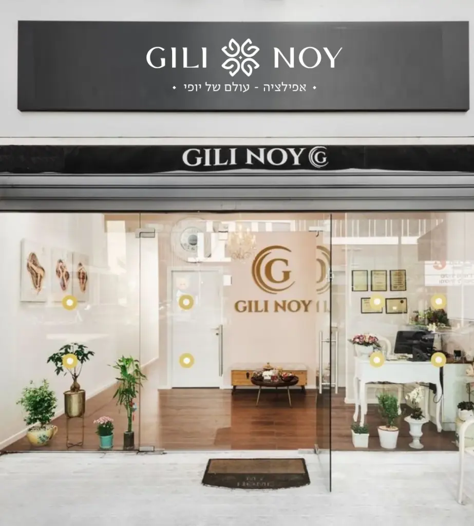 חזית חנות מודרנית עם השלט "GILI NOY" מעל דלתות הזכוכית ועציצים משני צדיה.
