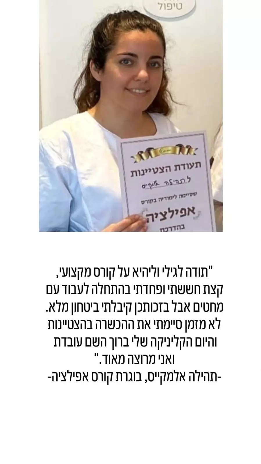 אישה מחייכת במעיל לבן מחזיקה תעודה עם טקסט בעברית, עומדת ליד קיר פשוט.