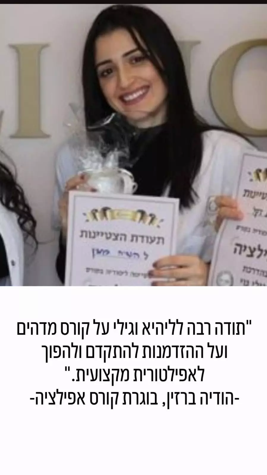 אישה מחייכת, אוחזת בתעודה, עומדת לצד אדם אחר על רקע אחיד.