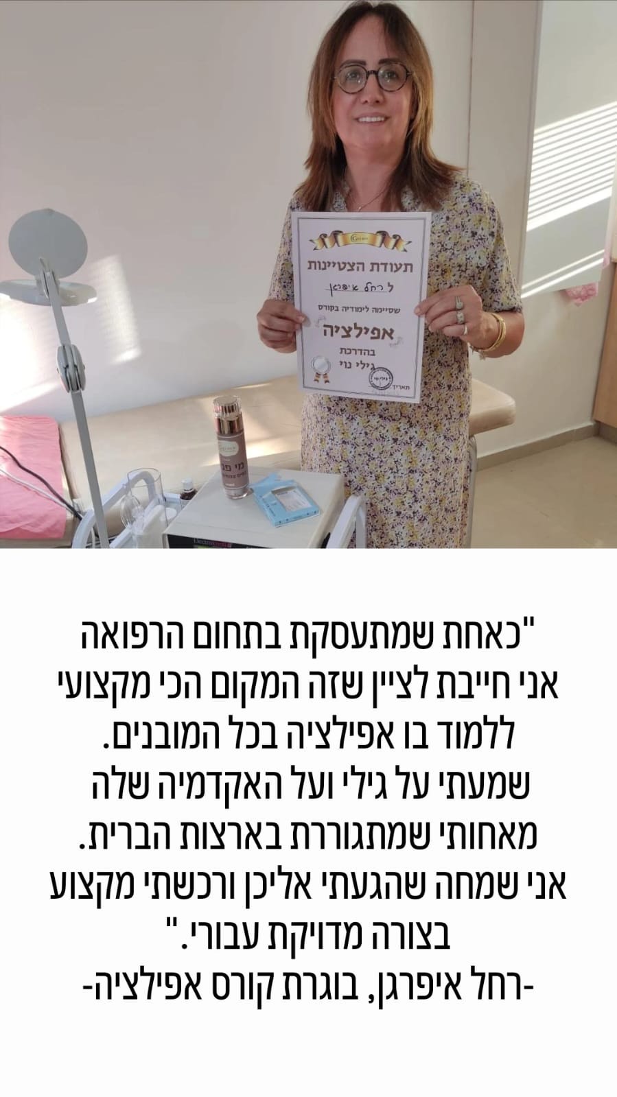 אישה מחייכת מחזיקה תעודה מודפסת בעודה עומדת בחדר בית חולים ליד מיטה וציוד רפואי.