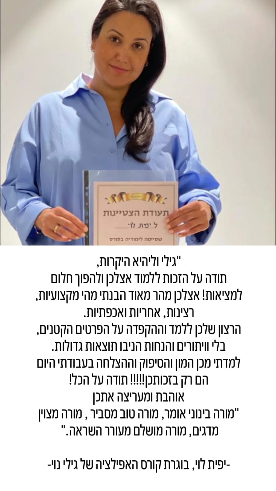אישה לבושה בכחול, מחזיקה תעודה ומחייכת, עומדת מול קיר שעליו כתוב טקסט בעברית המהווה עדות עליה.