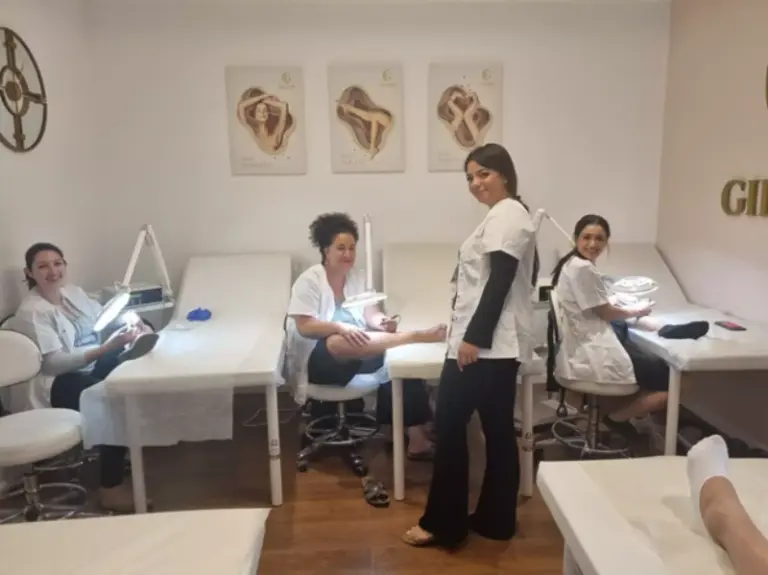 ארבע נשים במדים לבנים מעניקות טיפולי כפות רגליים בחדר ספא מסודר ומואר היטב, המעוטר ביצירות אמנות על הקירות.